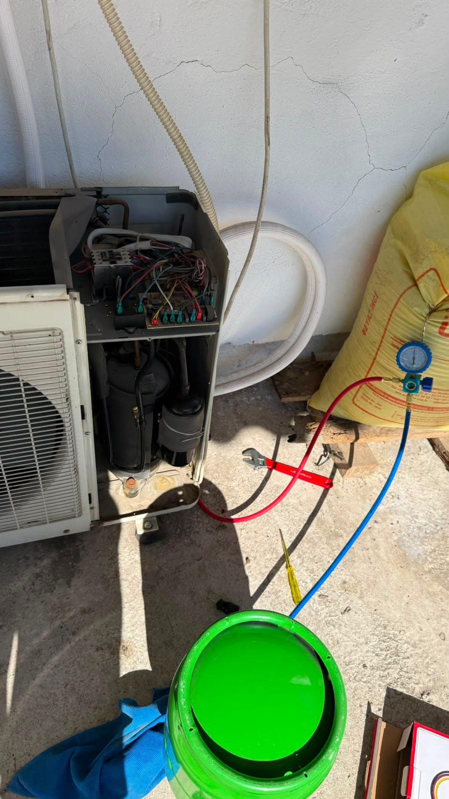 Kapağı sökülmüş dış ünite: elektronik kart, kablo demeti, kondansatör ve kompresör açıkta; servis vanalarına manometre bağlı, yerde İngiliz anahtarı ve pense duruyor