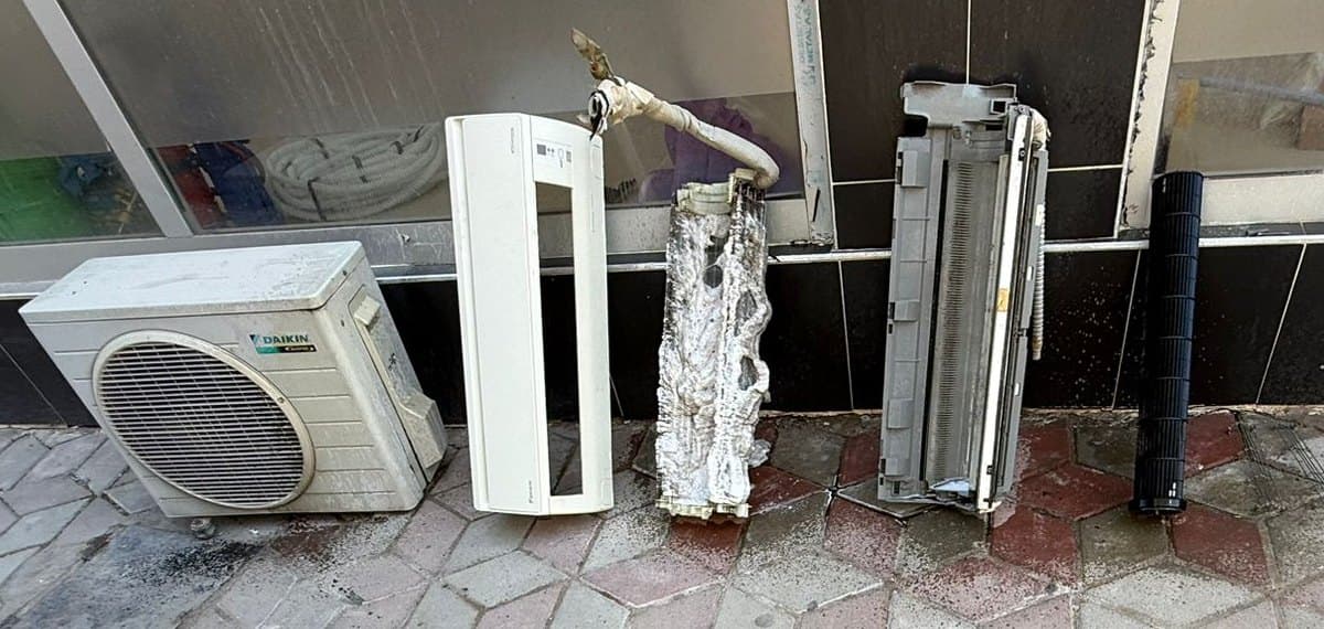 Derin temizlik için sökülmüş klima parçaları yan yana dizili: Daikin dış ünite, iç ünite ön kapağı, kireç ve kir tutmuş evaporatör bataryası ile siyah fan rotoru